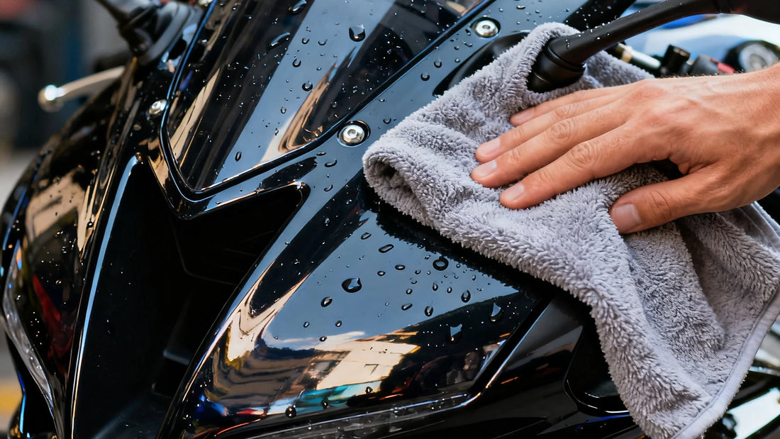 Close-up of a motorcycle fairing being cleaned with a microfiber towel, showing water droplets and glossy paint.